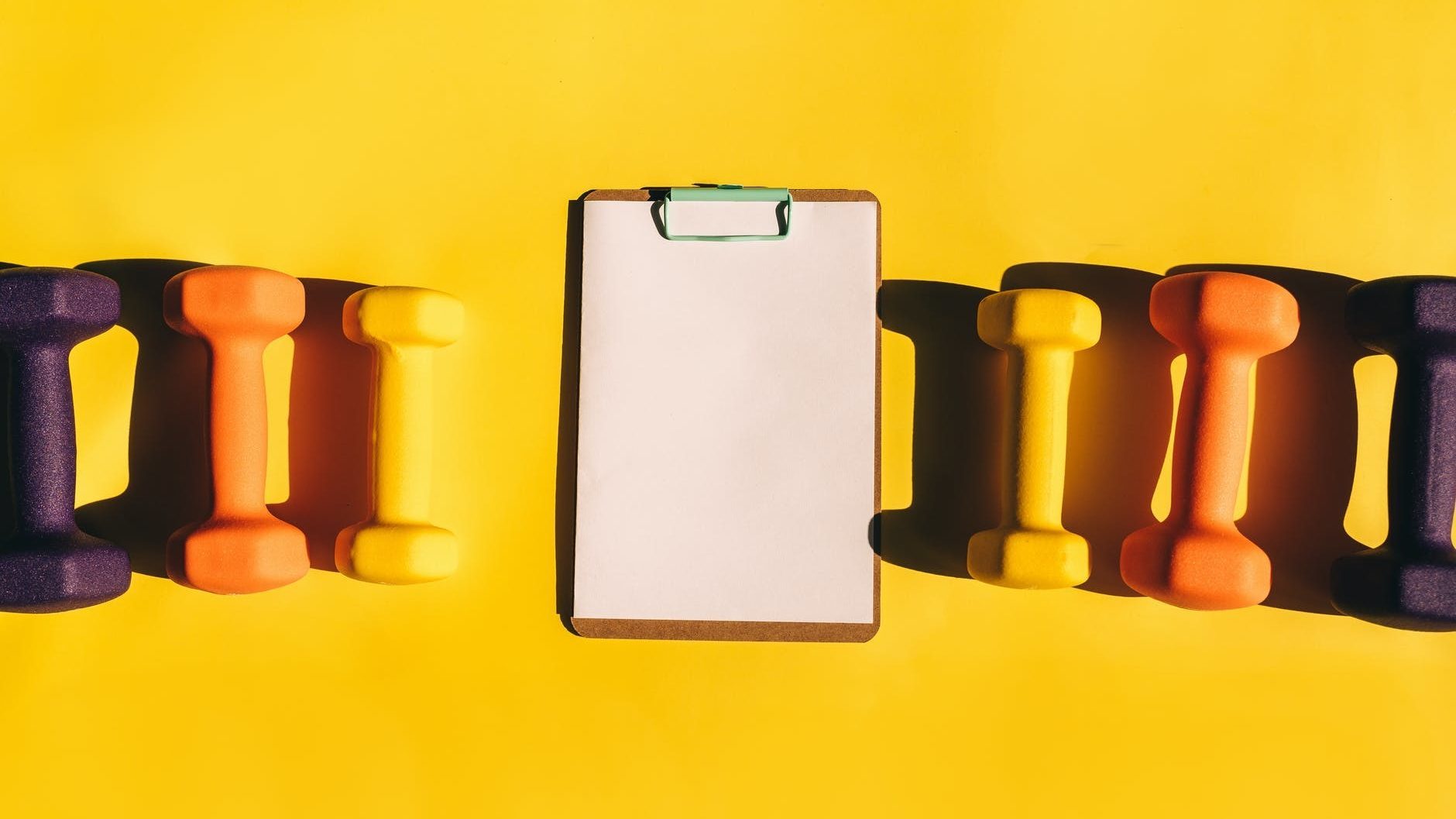 row of colorful dumbbells and a clipboard with a blank paper